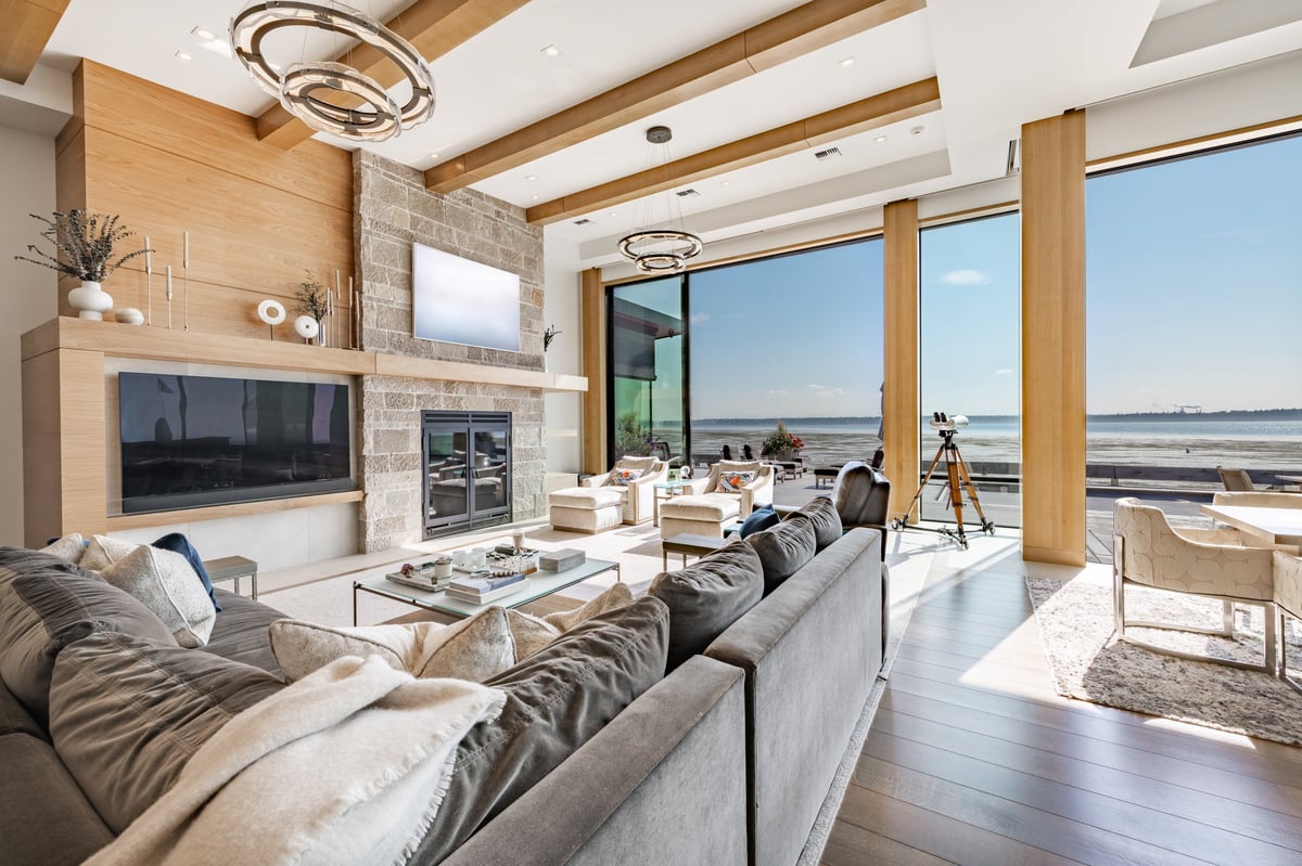Luxurious living room with floor to ceiling windows overlooking ocean, modern design with stone fireplace and panoramic views