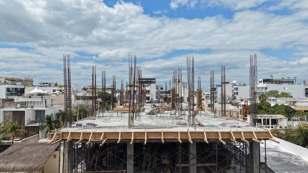 Construction site with exposed concrete structure and vertical steel reinforcement against urban skyline and cloudy sky