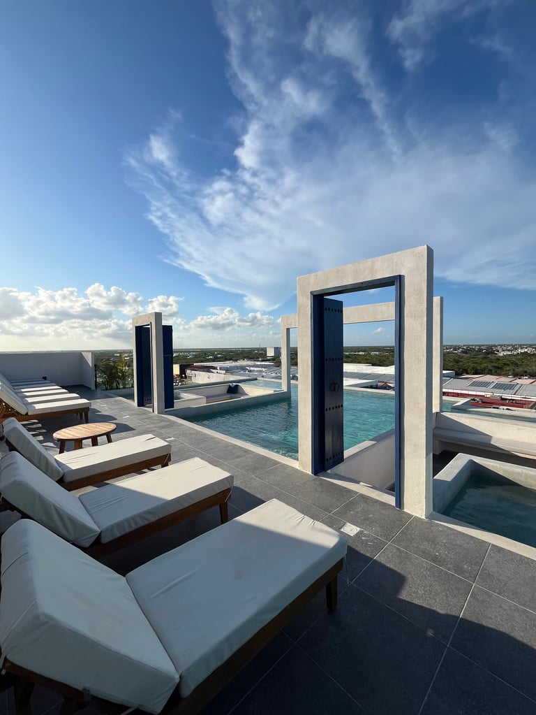 Modern rooftop pool with white loungers, concrete archway, and cityscape view under blue sky