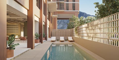Modern courtyard with narrow lap pool, terracotta buildings, loungers, and mountain views