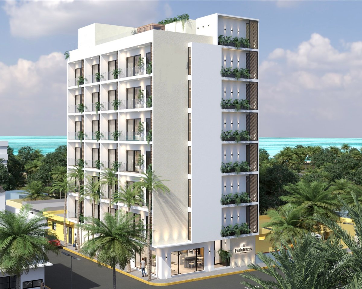 Modern white residential building with green balconies overlooking turquoise water and tropical vegetation