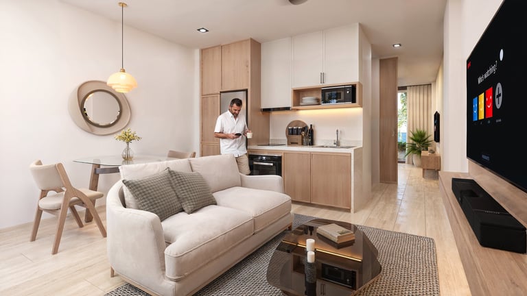 Modern studio apartment with open floor plan featuring beige sofa, wooden furniture, kitchenette, and natural lighting