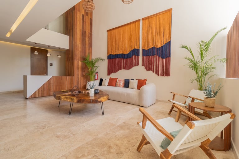 Modern living room with cream sofa, wooden furniture, potted plants, and colorful textile wall art on beige tiled floor