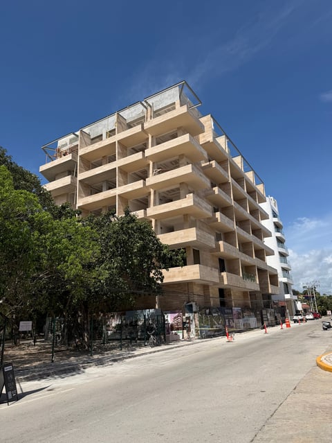 Modern multi-story apartment building under construction with concrete facade, balconies, and exposed framework against blue sky