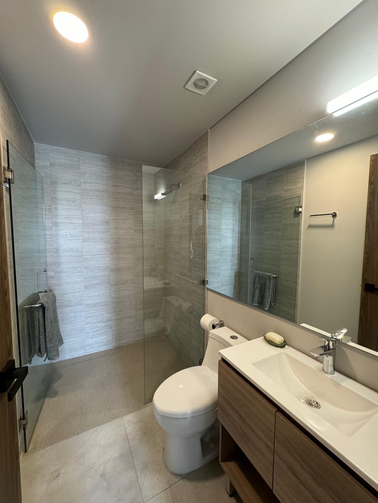 Modern bathroom with glass shower enclosure, white toilet, vanity with sink and mirror, and tile flooring