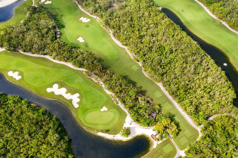 Aerial view of a golf course with multiple fairways, bunkers, and a winding river through forested landscape