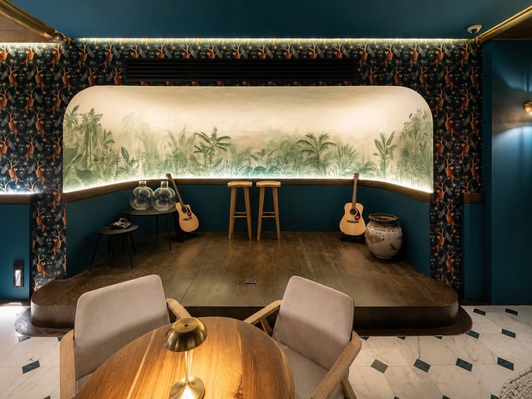 Modern music room with tropical mural backdrop, acoustic guitars, wooden stage, beige chairs, and teal patterned walls