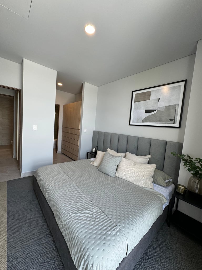 Modern bedroom with gray upholstered bed, white walls, framed art, and minimalist furnishings