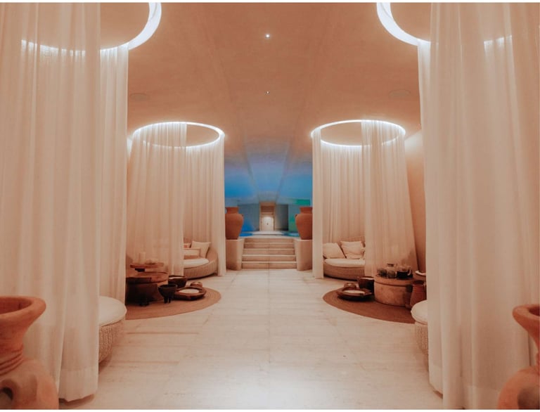 Modern spa interior with neon-lit cylindrical columns, flowing white curtains, terracotta walls, and minimalist seating areas leading to a blue-lit room