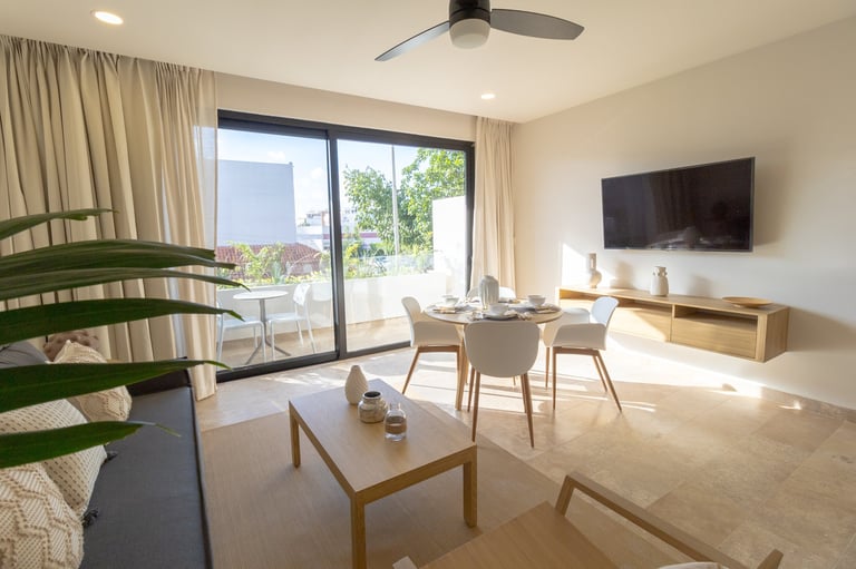 Modern apartment living room with dining area, wooden furniture, flat-screen TV, and sliding glass doors leading to a balcony