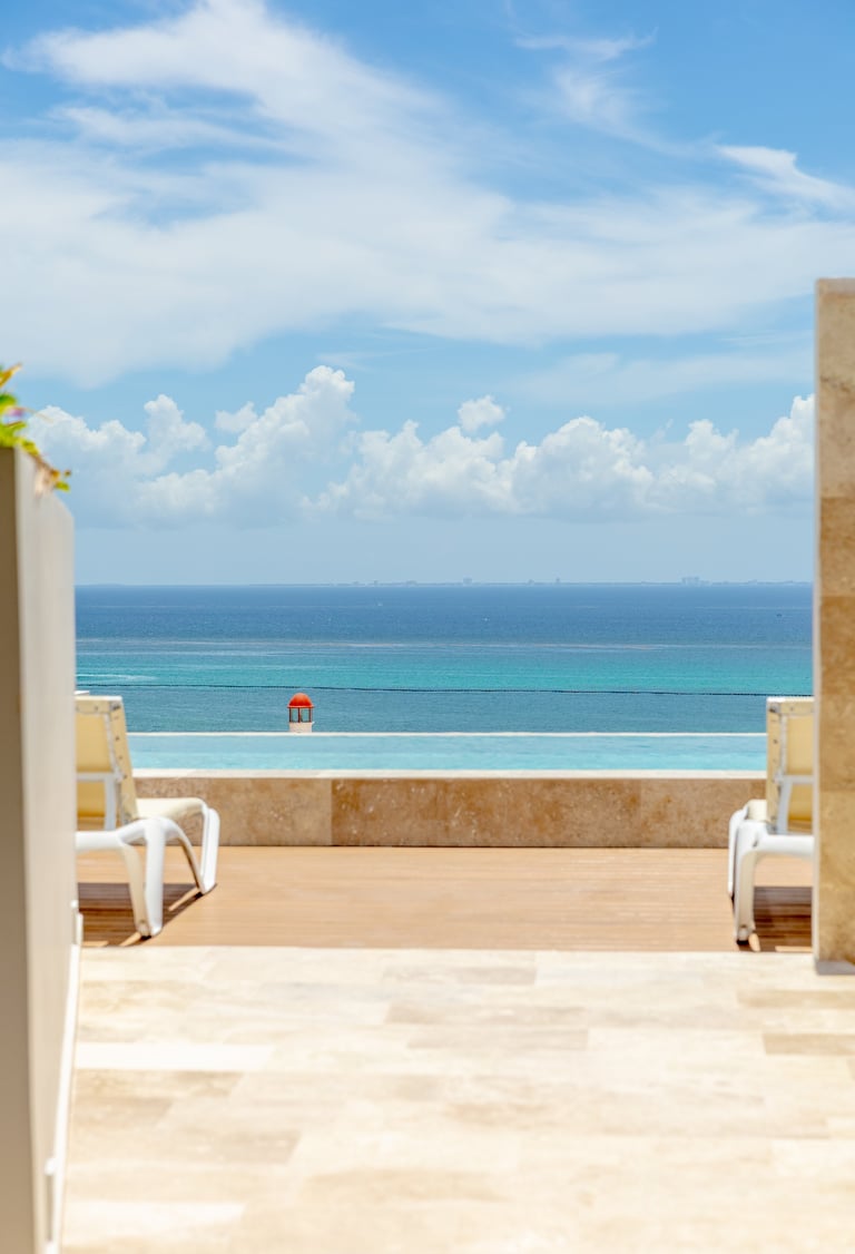 Luxurious seaside terrace with infinity pool overlooking turquoise ocean and blue sky with white clouds