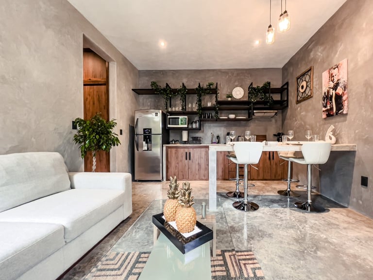 Modern studio apartment interior with white sofa, kitchen area, bar seating, and concrete accent walls