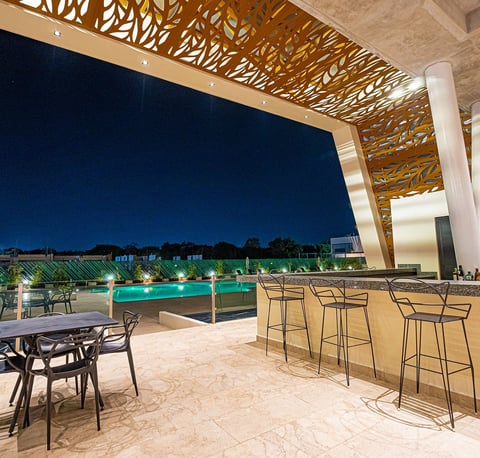 Modern rooftop bar with lounge seating overlooking illuminated swimming pool at night