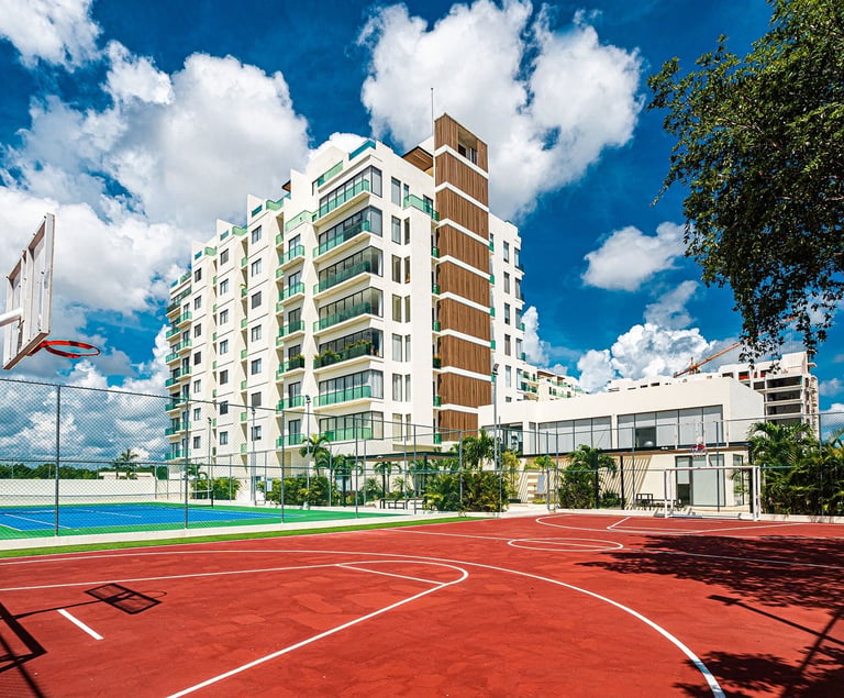 Modern residential apartment building with pool and red basketball court against blue sky with clouds