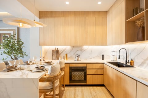 Modern kitchen with light wood cabinetry, white marble countertops, and an island dining area with place settings