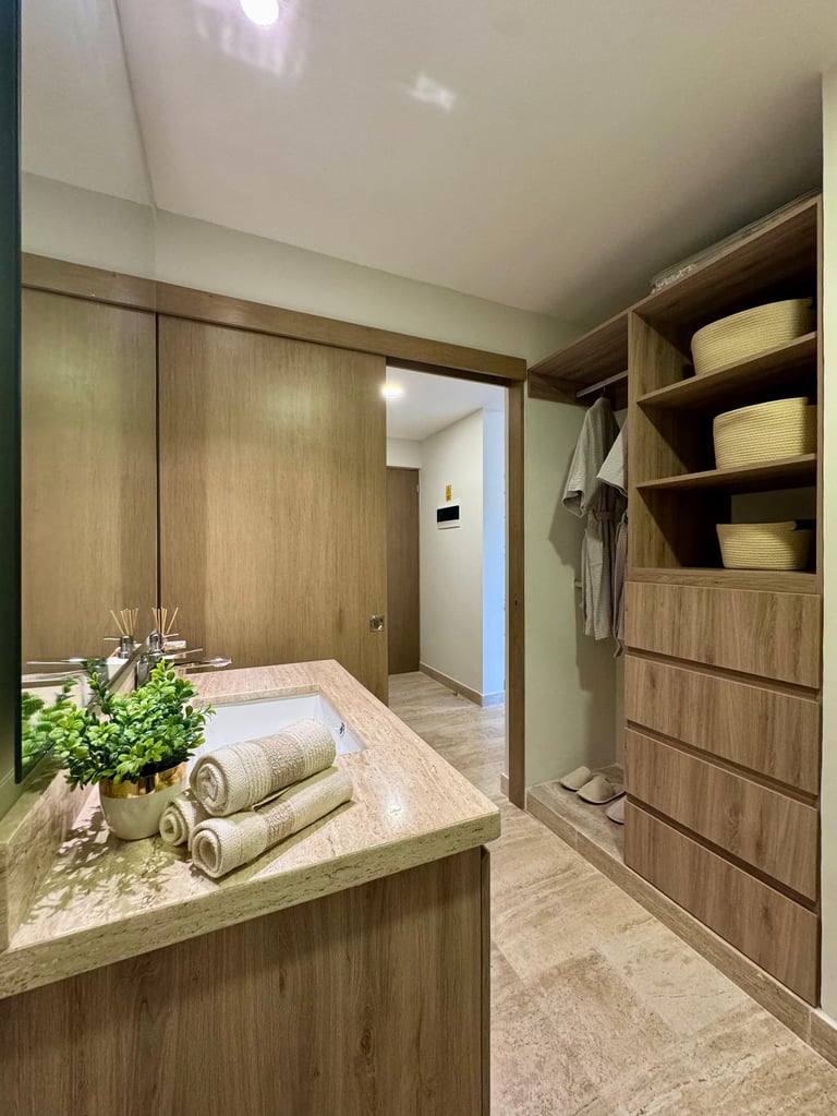 Modern walk-in closet with wooden cabinetry, island vanity with rolled towels, shelving unit, and neutral tones