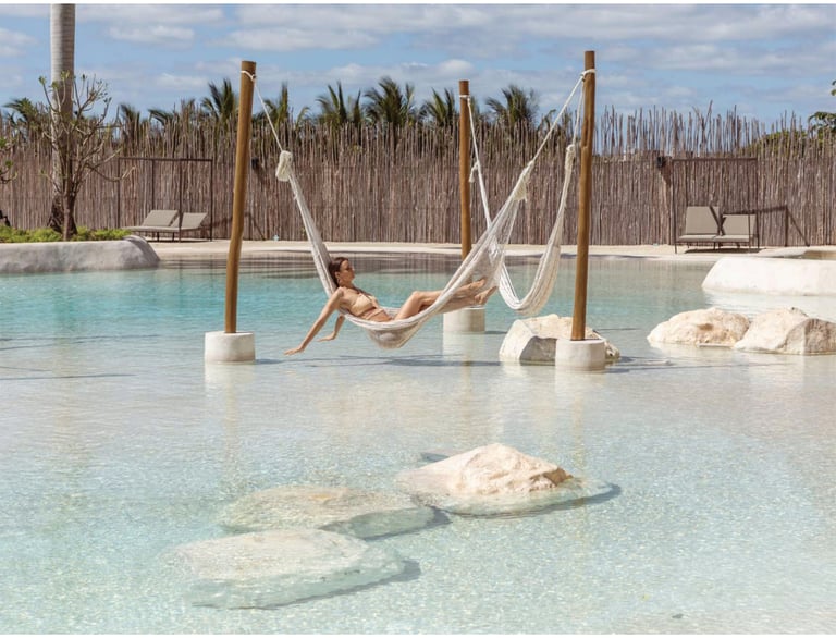 Woman relaxing in a hammock in shallow turquoise water at a luxury resort with thatched roof structures