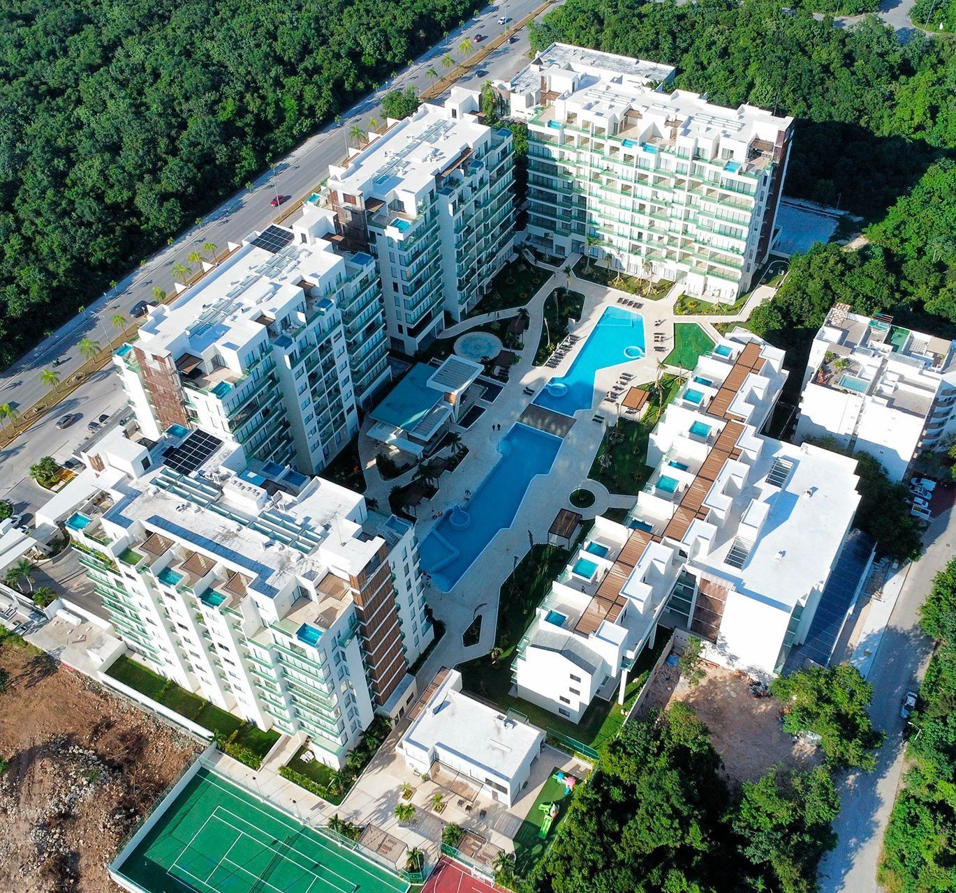 Aerial view of a large residential complex with modern apartment towers, blue swimming pool, and surrounding green spaces and forest