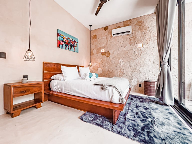 Modern bedroom with wooden bed, cork accent wall, pendant light, and blue area rug near large windows
