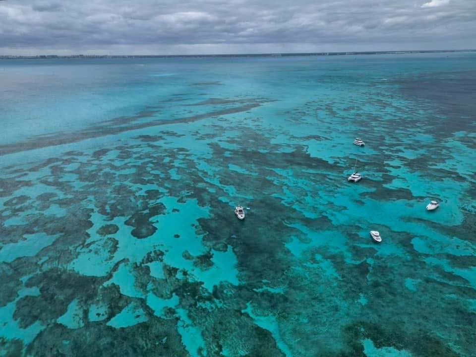 Aerial view of turquoise coral reef waters with several moored boats and dark coral formations beneath clear shallow waters