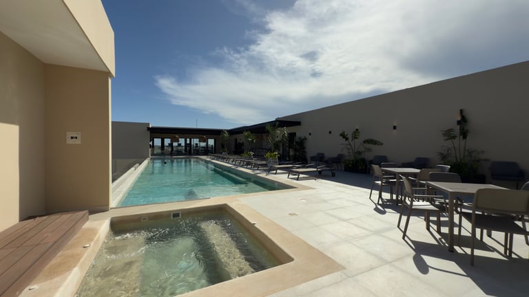 Modern backyard with rectangular pool, hot tub, lounge chairs, and dark wall under blue sky