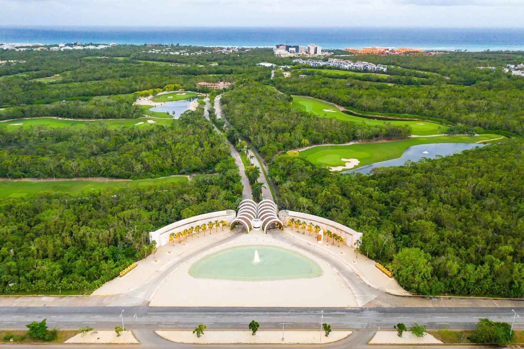 Aerial view of a large arched building with a central fountain overlooking a lush green landscape with winding roads and waterways
