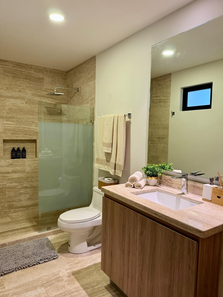 Modern bathroom with wood vanity, white sink, glass shower enclosure, beige tile walls, and recessed lighting