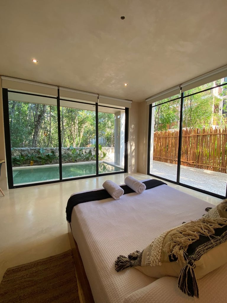 Modern bedroom with large glass sliding doors overlooking a pool and garden with natural light flooding the space