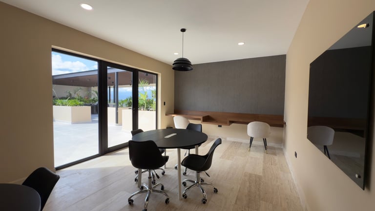 Modern minimalist home office with desk, black chairs, bed in background, and glass doors opening to patio with mountain views
