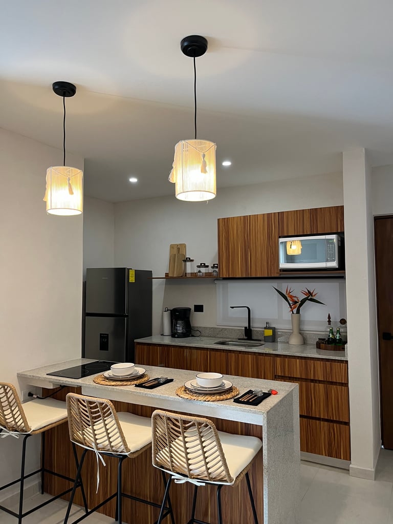 Modern kitchen with wood cabinetry, concrete countertop, pendant lights, and woven chairs at an island counter