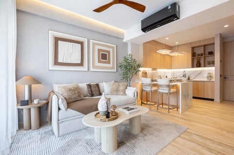 Modern open-concept apartment with beige sofa, wood coffee table, framed artwork, and kitchen with wooden cabinetry visible in background