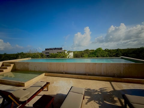 Rooftop terrace with large infinity pool overlooking lush tropical landscape and blue sky with white clouds