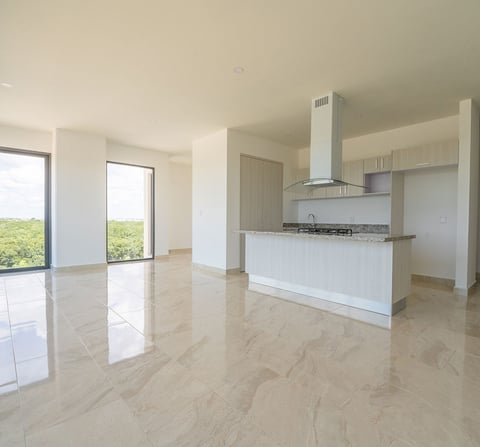 Modern open-plan kitchen and living area with marble flooring, white cabinetry, stainless steel range hood, and large windows overlooking greenery