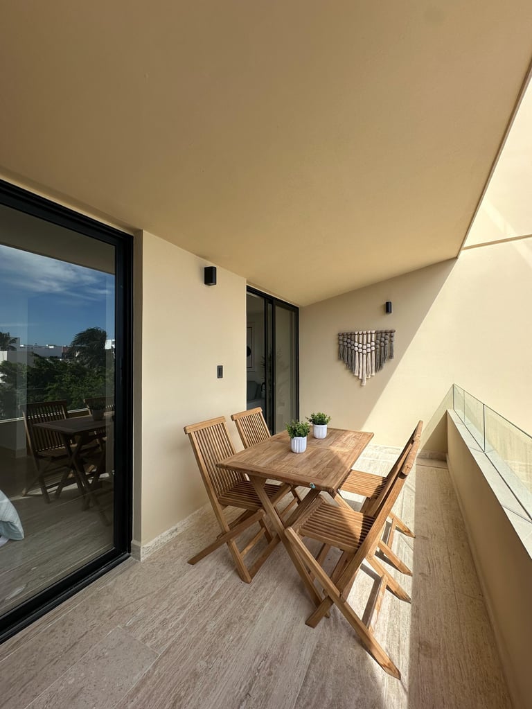 Modern balcony with wooden dining table and chairs, white walls, large glass door, and scenic city view