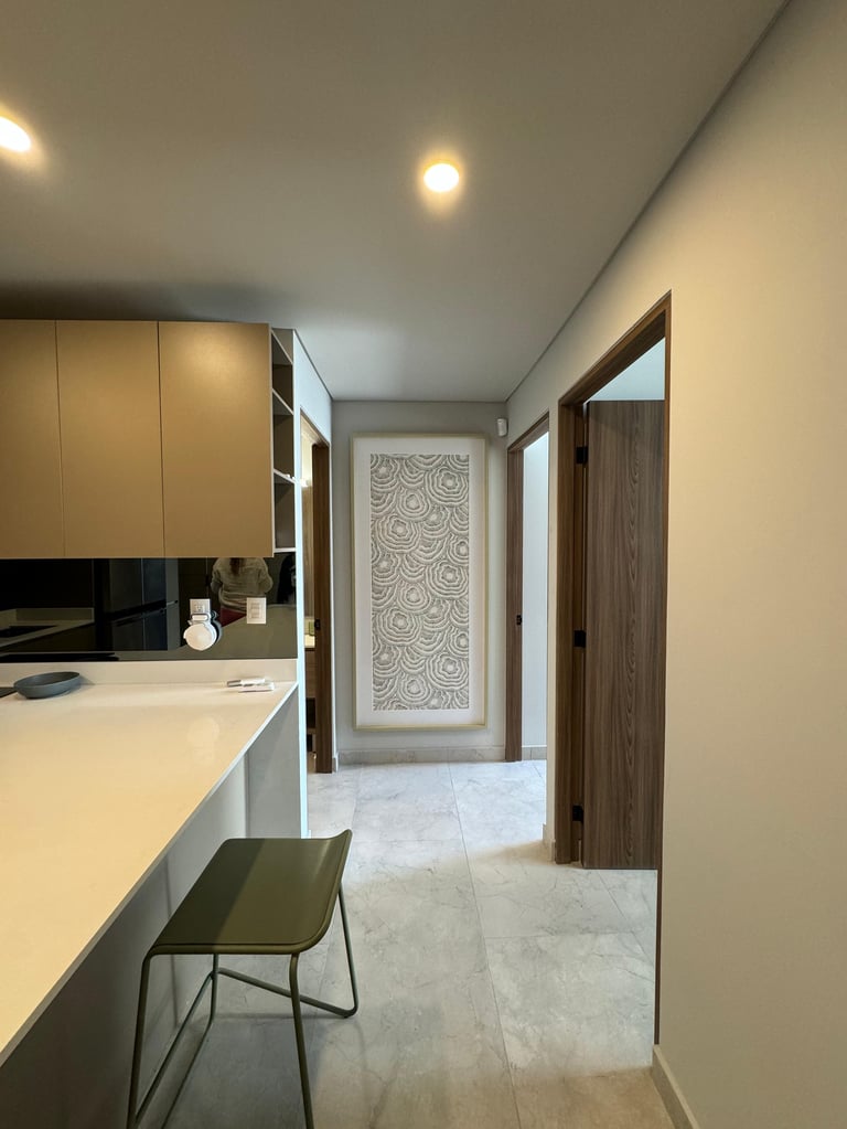Modern kitchen with cream cabinetry, white countertop, black bar stool, and hallway with decorative wall art