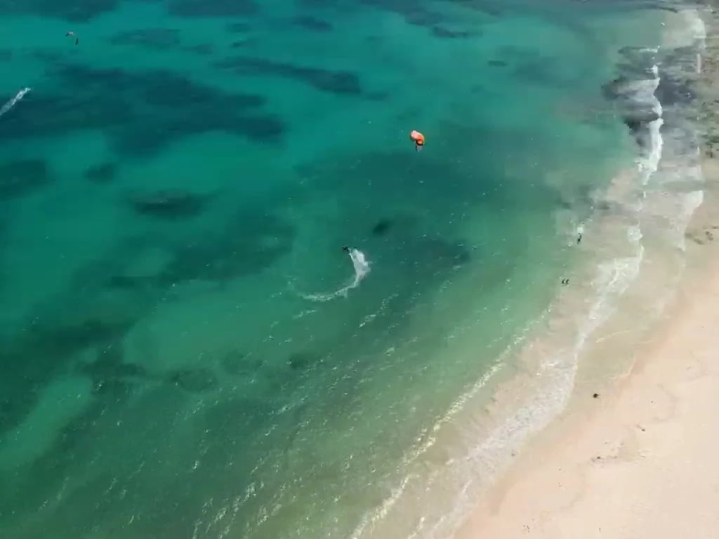 Aerial view of two swimmers in turquoise water near a sandy beach with white waves