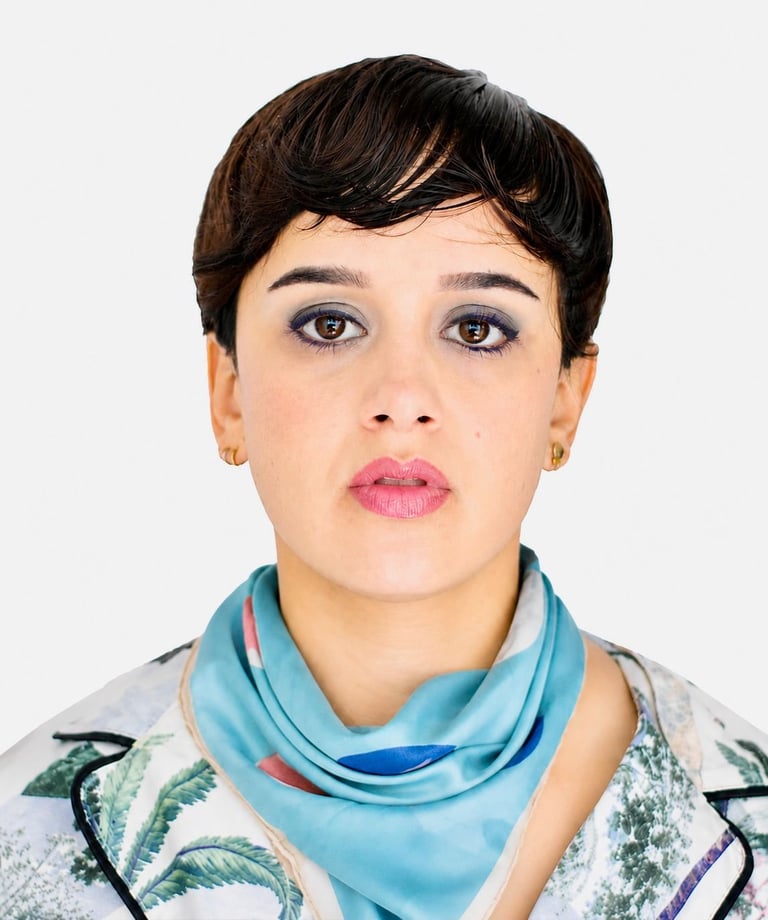 Portrait of a person with short dark hair, blue eyes, and pink lipstick wearing a blue scarf and patterned shirt against a white background