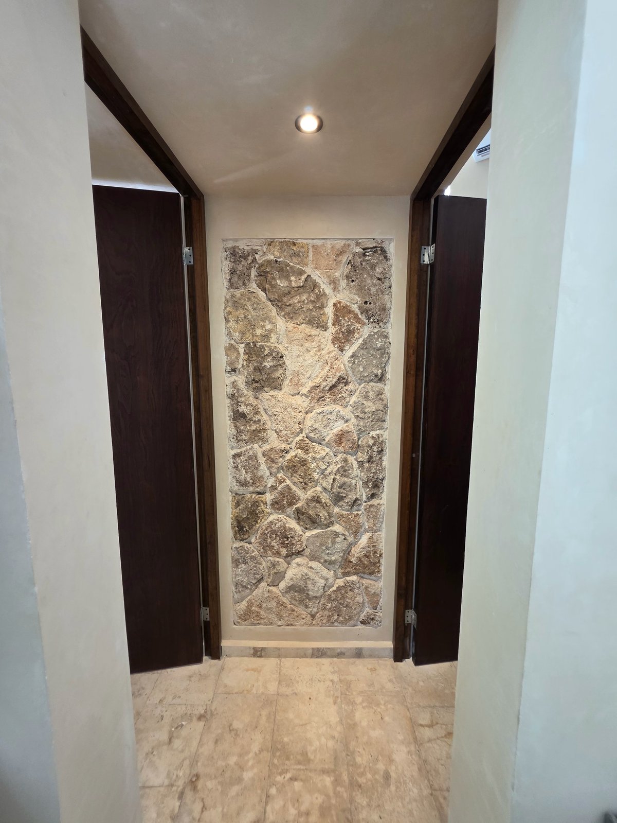 Narrow bathroom entrance with black framed glass shower door, marble tile flooring, and stone tile shower wall