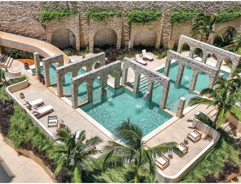 Aerial view of a luxury resort pool with turquoise water, lounge chairs, palm trees, and Mediterranean-style stone archways
