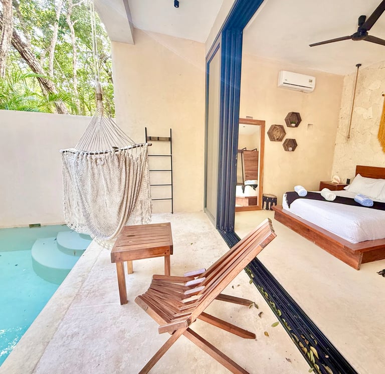 Modern bedroom with open-air patio, hammock, wooden deck chairs, pool access, and coastal-style furnishings