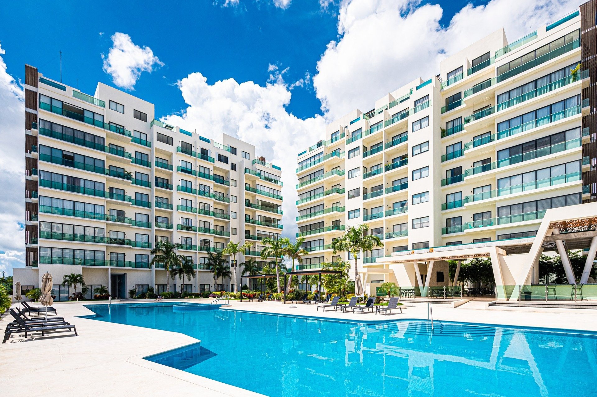Modern apartment complex with large outdoor swimming pool and palm trees under blue sky