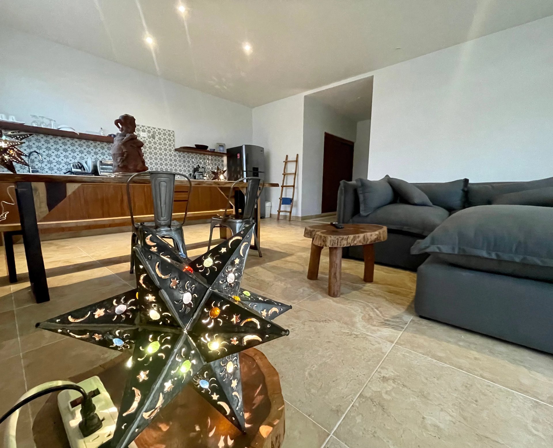 Modern open-plan living room with decorative star lights, wooden kitchen, gray sectional sofa, and concrete floors