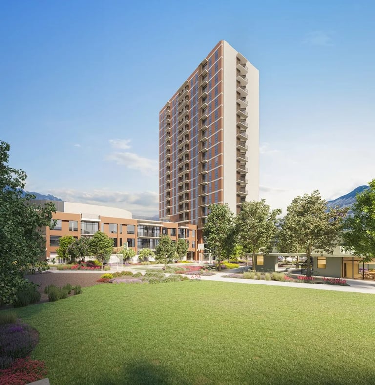 Modern residential complex with tall apartment tower and low-rise building surrounded by green lawn and landscaping against mountain backdrop