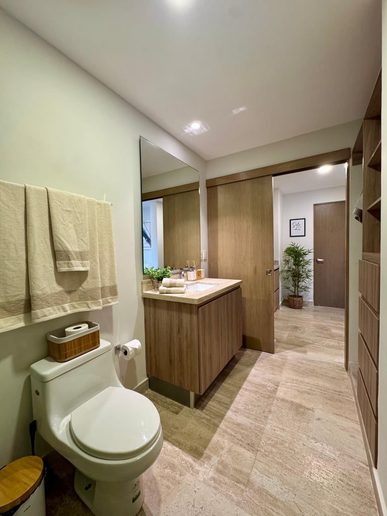 Modern bathroom with wood vanity, white toilet, large mirror, yellow towels, and wood-look flooring
